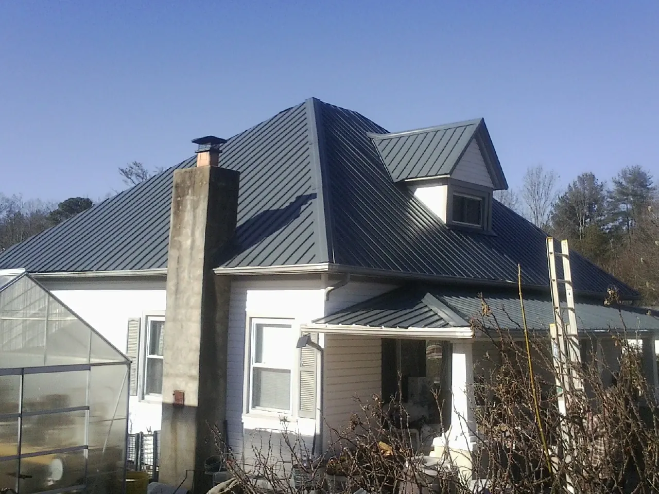 Dark blue standing seam metal roof on a white farmhouse with dormer — Slate & Tile Roof Repair by Roofing Brothers in Brownsville