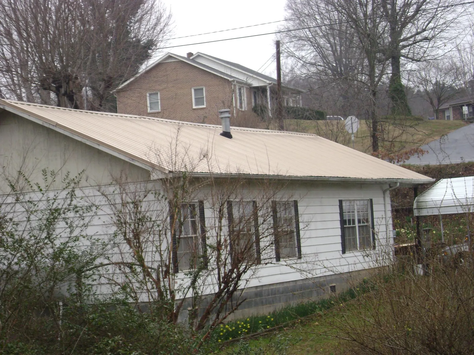 Tan metal roof on a white sided house set into a hillside — Commercial Roofing by Roofing Brothers in Brownsville